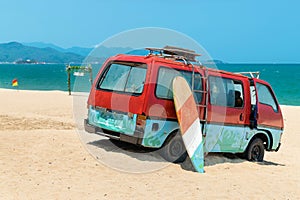 Old bus in the sand and a surfboard on the beach