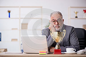 Old male employee being awarded with golden cup