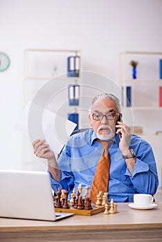 Old businessman playing chess at workplace