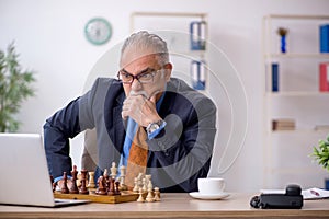 Old businessman playing chess at workplace