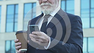 Old businessman using phone at coffee break, scrolling photos in social network