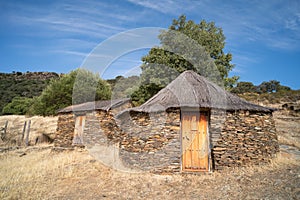 Old cabin or hut with a round shape and slate stone walls and a broom and straw roof