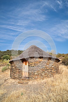 Old cabin or hut with a round shape and slate stone walls and a broom and straw roof