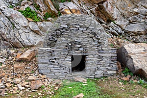 Old cabin or hut with a round shape and slate stone walls and a broom and straw roof