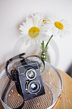 Old camera with a bouquet of daisy flowers on a wooden board