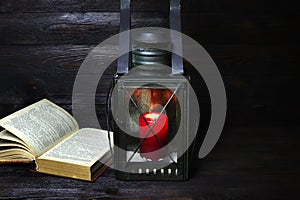 An old candle lantern and book on a wooden background. Old lamp with a burning candle .Christmas lamp