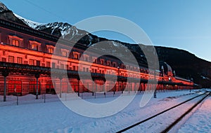 Old Canfranc train station with the facade illuminated in reddish tones on a winter night with snow on the tracks, Huesca, Spain