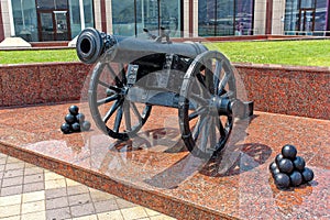 An old cannon on wooden wheels and cannonballs nearby