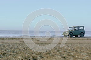 Old car parked on sandy beach near ocean shore