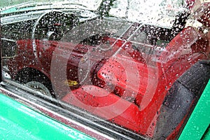 Old car. Red chairs and wheel. The window is covered by raindrops