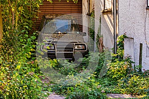 An old car stands neglected in an overgrown yard of a neglected house