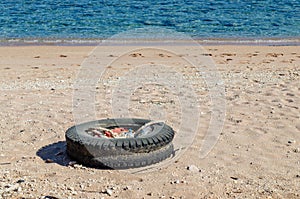 An old car tire and plastic waste are lying on the sandy seashore