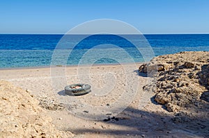 An old car tire and plastic waste are lying on the sandy seashore