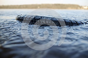 Old car tire thrown into the river. Concept of environmental pollution
