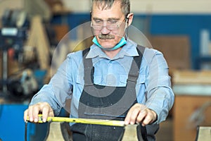 An old carpenter with a mustache and glasses is concentrating on his work.