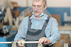 An old carpenter with a mustache and glasses is concentrating on his work.