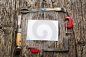 Old carpenter tools on rustic wood table with blank paper top view.