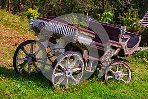 An carriage made of wood with large wheels without a horse on a mountainside on green grass. Retro and vintage from the story