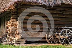 Old cart with wooden wheels against the background of a log house under thatched roof