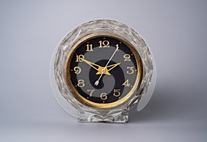 Old carved glass clock with black dial and golden hands and numbers. Frontal view of the face of a shabby vintage clock