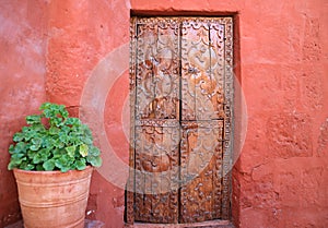 Old carved wood door on the orange red color rough wall with a big terracotta planters in Santa Catalina Monastery