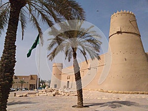 Old castle in Riyadh near the Municipality, national flag of Saudi Arabia Kingdom in front of castle towers , palms around