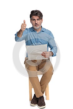 Old casual man reading a newspaper and giving thumbs up