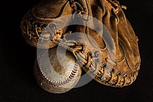 Old catchers mitt and worn baseball on black backdrop