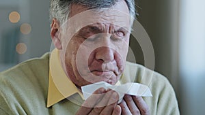Old Caucasian 60s man sick suffering aged mature senior ill 70s male patient grandfather sneezes runny nose wipes snot