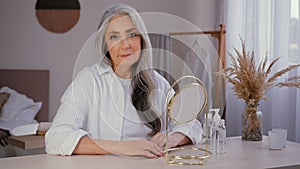 Old Caucasian gorgeous lady 60s female smile senior mature woman with mirror at home looking at camera grandmother 50s