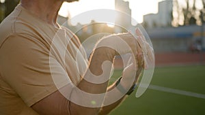 Old Caucasian man stretch hands before training warm-up stadium outside city sportsman sport lifestyle sunray stamina