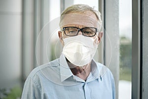 Old Caucasian man is wearing medical mask , looking to outside his home