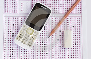 Old cell phone,wooden pencil and rubber on filled exam shee