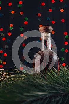 Old cellar dusty bottle of brandy, scotch, whiskey, cognac on blurry Christmas garland lights bokeh background, green pine