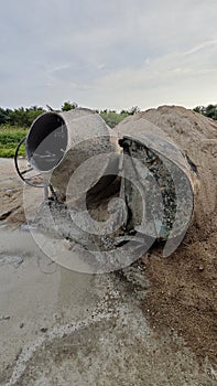 an old cement mixer machine by the pile of sand at the construction site.
