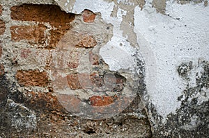 Old cement wall cracked to reveal red bricks inside, poor quality construction