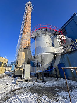 An old ceramic chimney and an new flue gas dust collector behind a coal boiler, a grate, against the blue sky