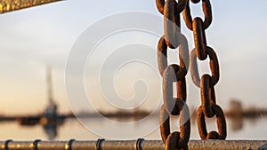 The old chain by the pier at sunset. Defocused background with ship and dramatic sky. Adventure concept