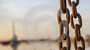 The old chain by the pier at sunset. Defocused background with ship and dramatic sky. Adventure concept