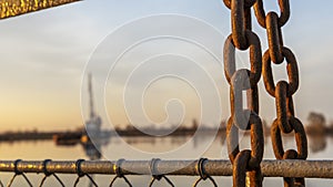 The old chain by the pier at sunset. Defocused background with ship and dramatic sky. Adventure concept