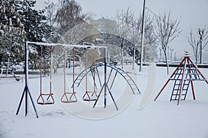 Old children playground, slides and swings, in a park covered in snow in Serbia, in Eastern Europe, during a freezing dark evening