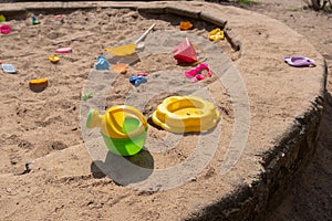 an old children's outdoor sandbox with a children's watering can in the foreground and a bunch of forgotten toys