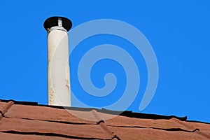 Old chimney of asbestos pipe over a rusty metal roof