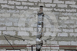 old chimney pipe in gray insulation at the brick wall of the building