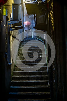 An old Chinese lady with an umbrella in a mysterious back alley and staircase in the Taiwanese village of Jiufen