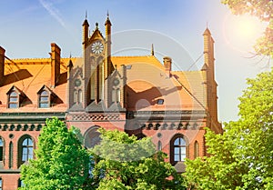 The old church is illuminated by the sun, the beautiful landscape of the brick building behind the trees