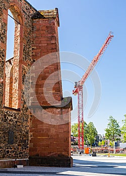 Old church walls and construction crane. Construction next to the church. City infrastructure. Under the blue sky.