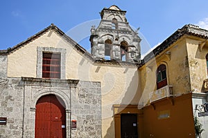 Old church with wooden entrance door framed by stone facade and bell tower on a sunny day in Old Town, Cartagena, Colombia
