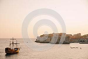 The old city of Dubrovnik against the sunset sky. The wooden sailing ship Galleon approaches the main pier of Dubrovnik.