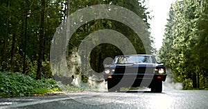 Old classic car is moving on countryside road in forest in daytime, frontal view from ground